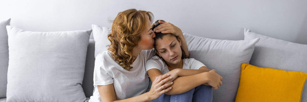 Letter to My Daughter With Anxiety Mom giving daughter kiss on forehead as they snuggle on couch