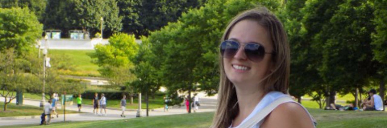 Internal Morning Dialogue of Someone With Depression young woman posing on grassy hill in front of trees and monument