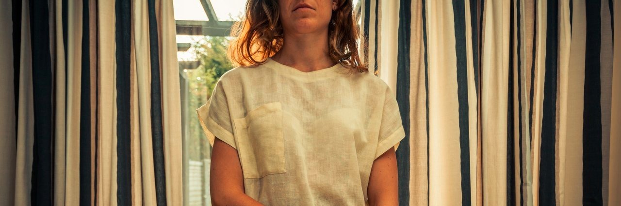 Saying ‘You Look Great’ Can Hurt People With Chronic Illnesses Young woman standing by curtains of french doors