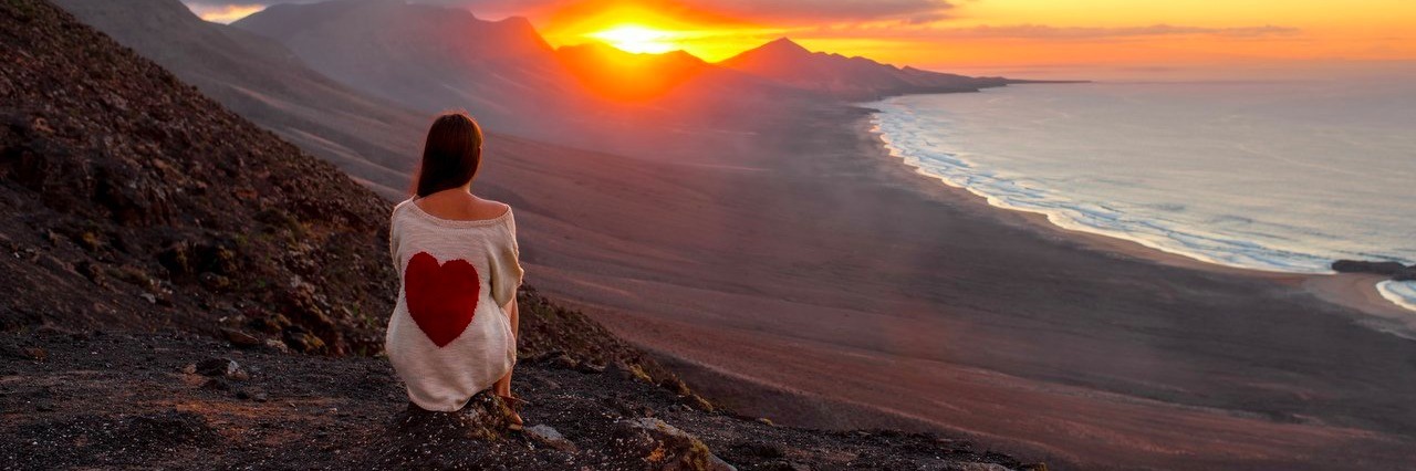 woman watches sunset while sitting on a mountain