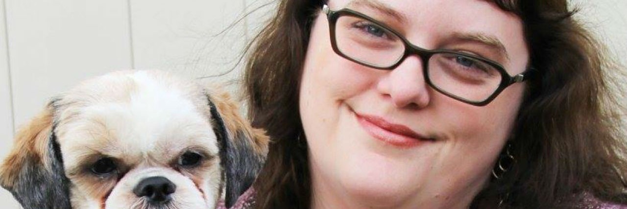 The 'Weird' Thing That Brings Me Solace When Anxiety Takes Over a woman wearing a purple sweater and glasses holding her dog