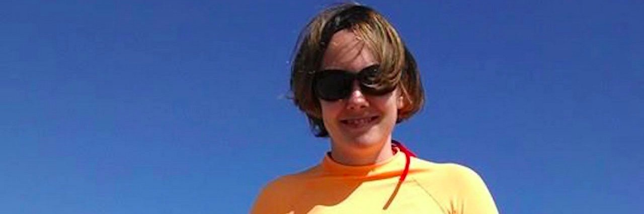 Woman Discusses What People Misunderstand About Her Epilepsy woman on a beach holding a bodyboard