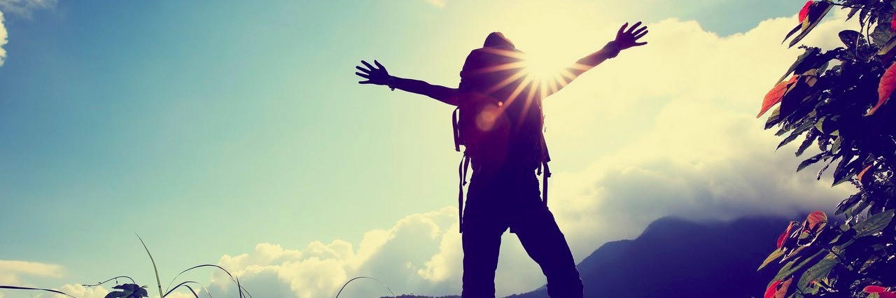 hiker open her arms on mountain peak at sunrise