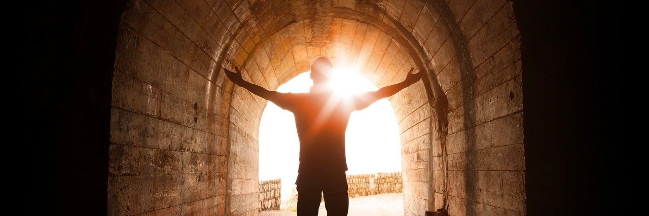 Man stands inside of dark tunnel with sun shining in
