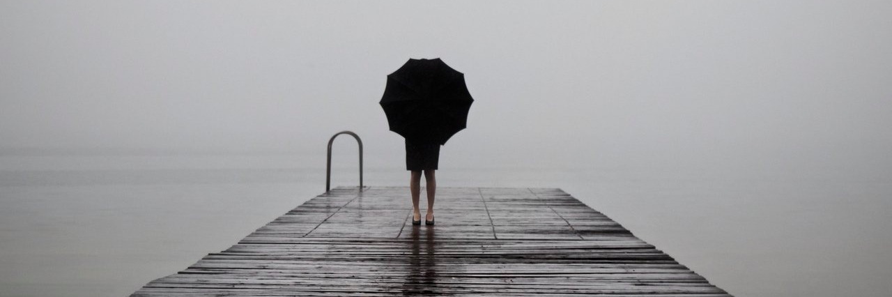 Chronic Illness: Coping With a Loss of Identity After a Diagnosis woman dressed in black with an umbrella in a misty landscape