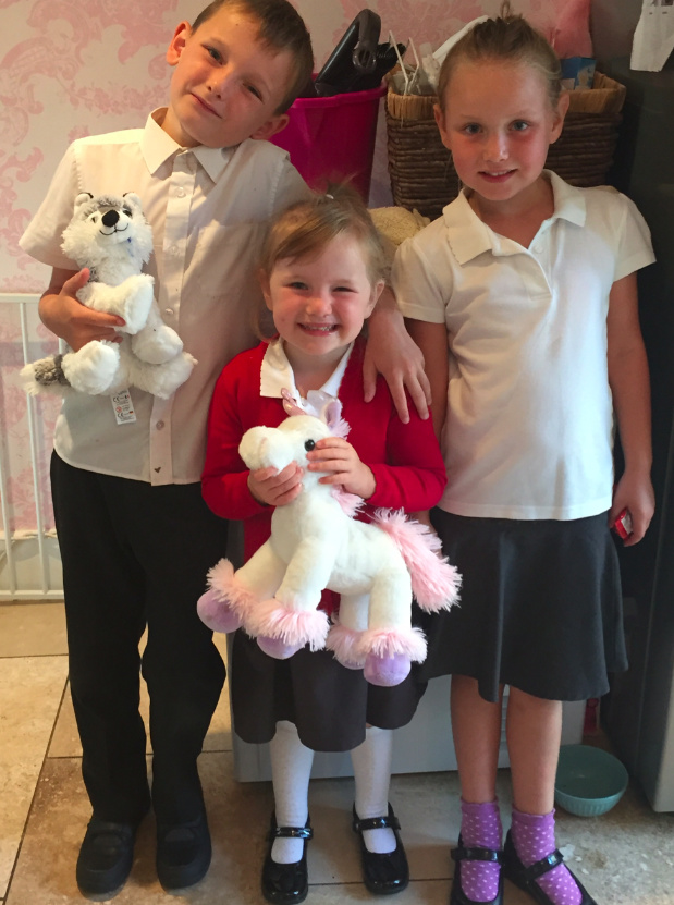 Three kids wearing school uniforms, two of them holding stuffed animals