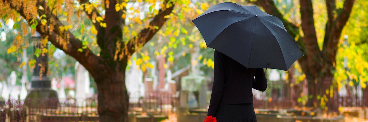 a woman dressed for a funeral holding an umbrella standing in a grave yard.