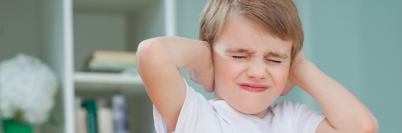 Frustrated boy covering his ears with hands at home