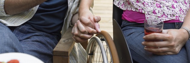 Couple with woman in wheelchair holding hands.