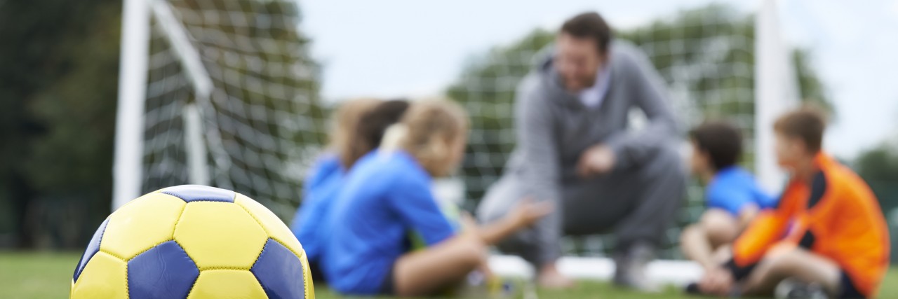 Choosing to Mainstream My Son With Down Syndrome in Gym Class Coach And Team Discussing Soccer Tactics With Ball In Foreground