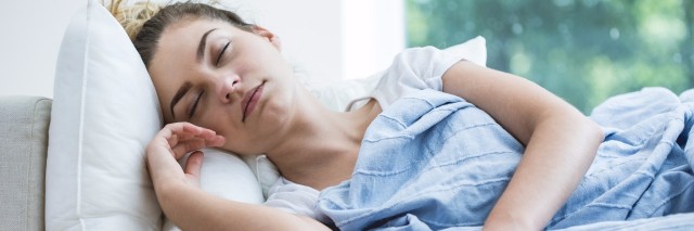 Feverish woman lying under blanket with thermometer