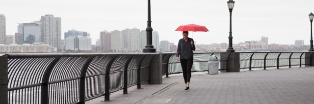 Woman walking on bridge, holding red umbrella