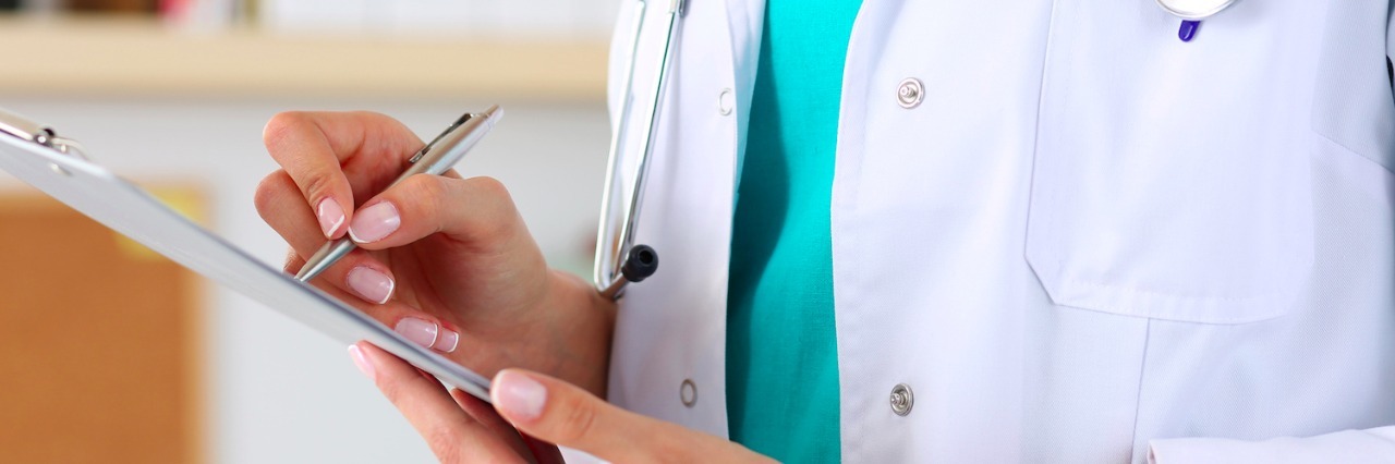 When I Was Diagnosed With Bronchiectasis After Years of Chest Problems Doctor holding silver pen, writing on a clipboard