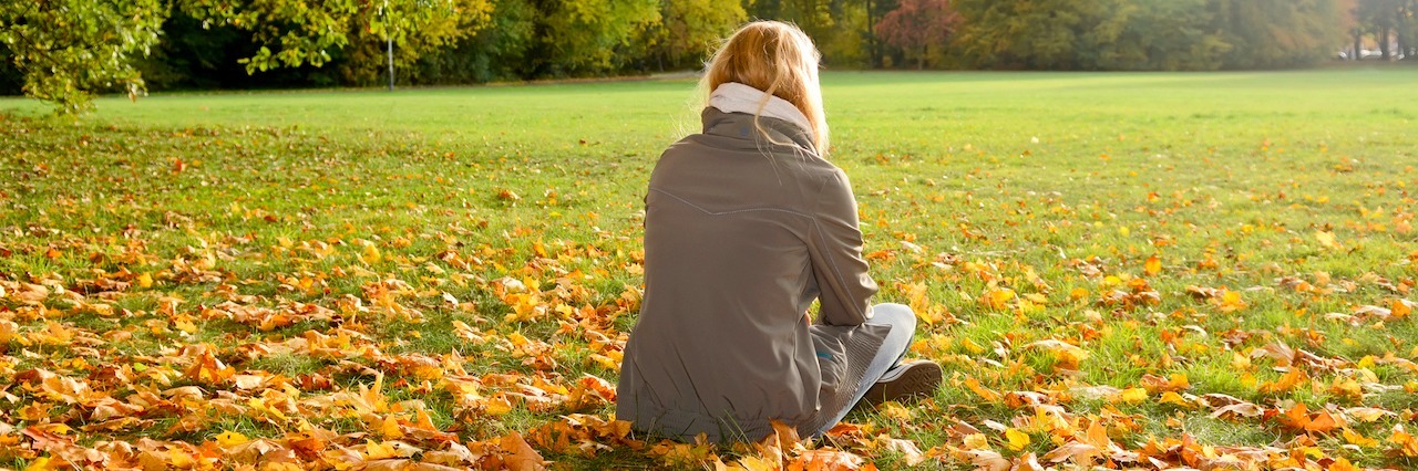 lonely young woman sitting in autumn park, rear view