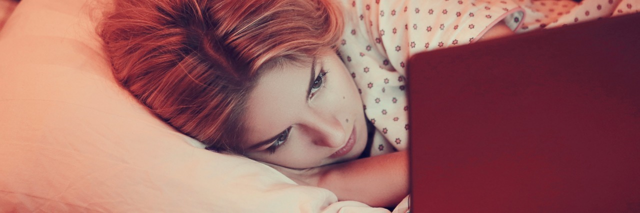 girl lying in bed looking at laptop