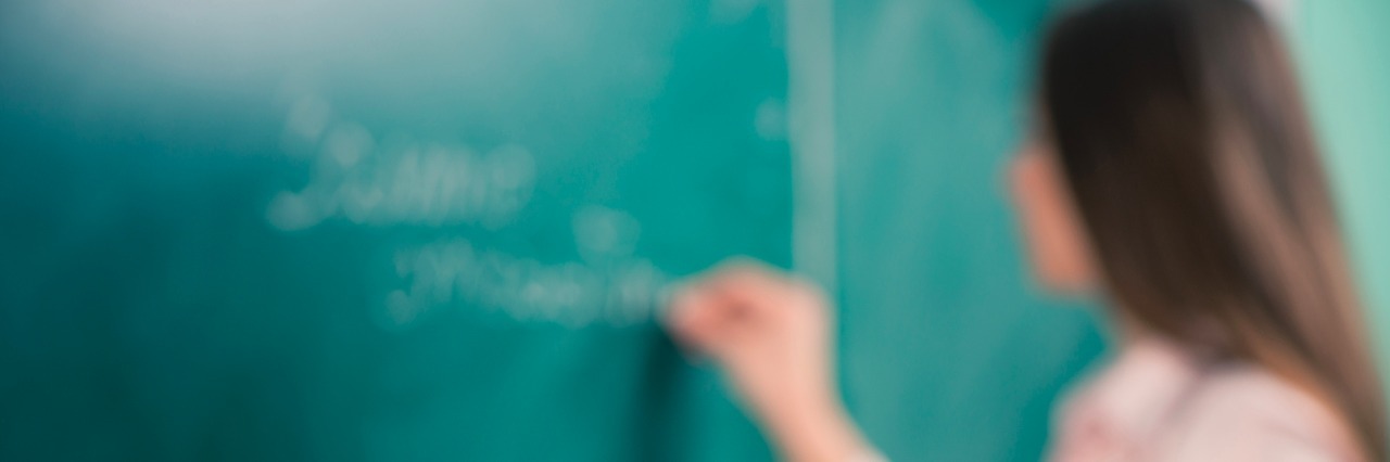 Switching Jobs Because of My Chronic Illness glasses and books at the classroom table while teacher writing on a blackboard