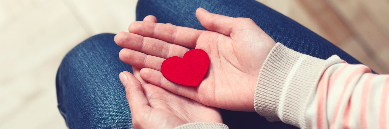 Why You Should Keep Dating With a Chronic and Rare Illness Girl is sitting and holding red heart in her hands on lap. Love and relationships concept