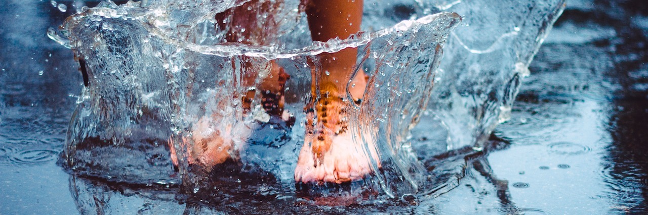 a girl wearing sandals jumping in a puddle