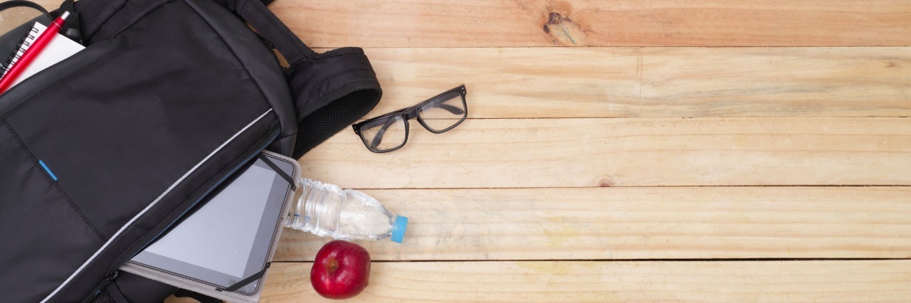 Lessons Learned as My Son on the Autism Spectrum Starts Middle School Backpack next to red shoes and glasses on a wood floor