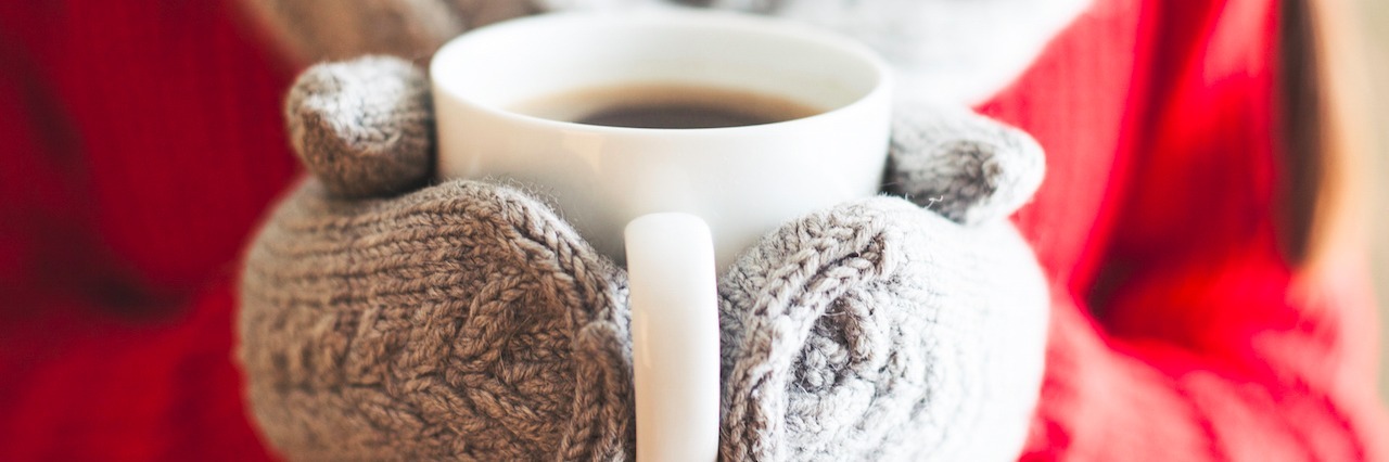 Female hands holding hot mug close up. Woman hands in woolen mittens holding a cup with hot cocoa, tea or coffee.