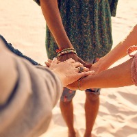 group of friends putting their hands together at the beach