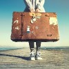 woman holding old, tattered suit case standing on a doc