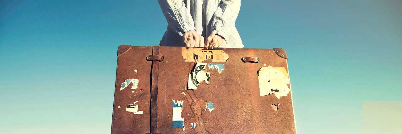 woman holding old, tattered suit case standing on a doc