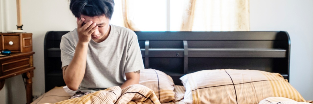 What 'Migraine Brain Fog' Feels Like Photo of man sitting in bed, with one hand over half of his face