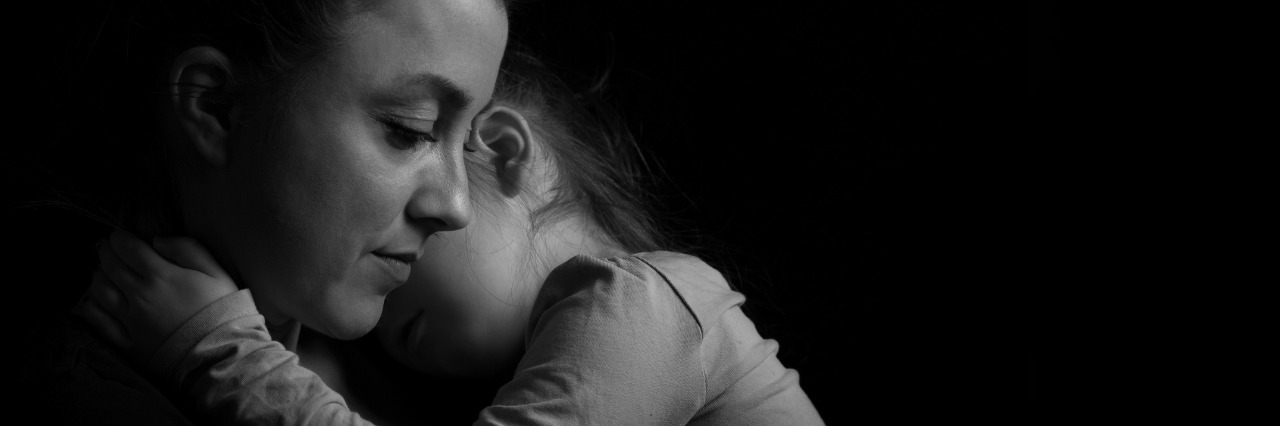 Why Moms Aren't Asking for Mental Health Treatment black and white picture of a mother holding her child against her chest in front of a black background