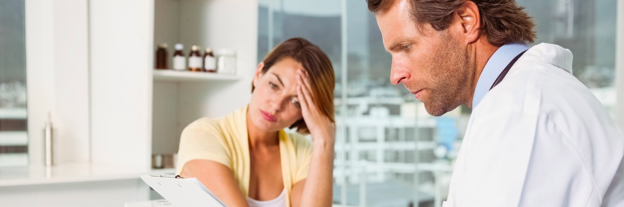 Male doctor discussing reports with patient at desk in medical office