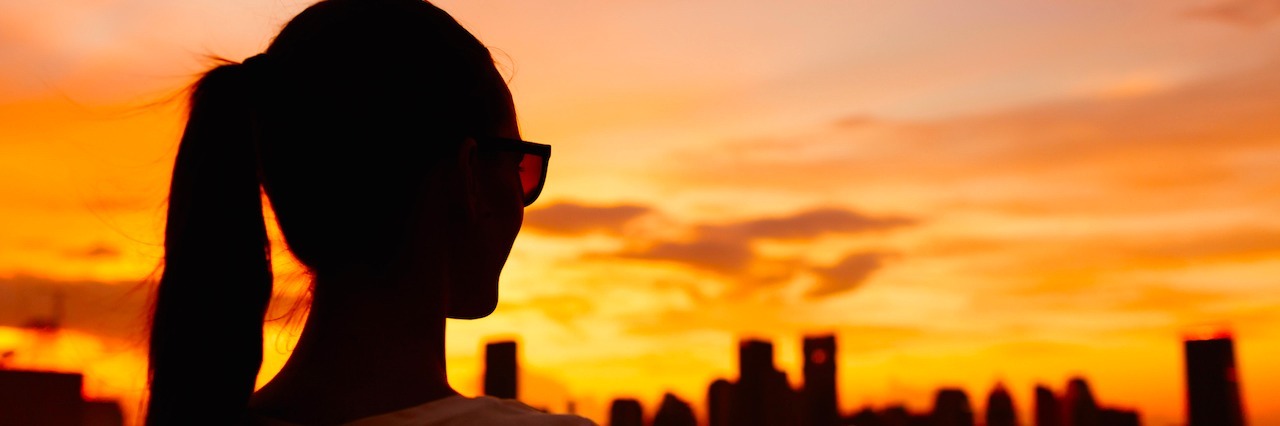 silhouette of woman looking at sunset over city skyline