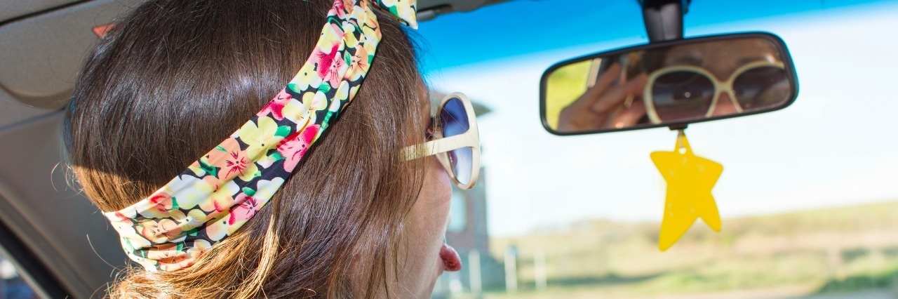 young woman driving a car and looking at herself in the mirror