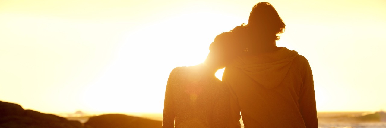 Portrait from behind of loving couple holding hands at the beach and watching the sunset