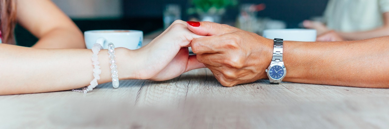 Two women holding hands on a wood table