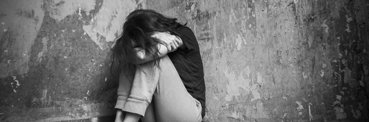 sad girl sitting on the floor in corner of a room with her head resting on her folded arms