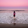 Woman standing in the ocean in front of a pink and purple sky