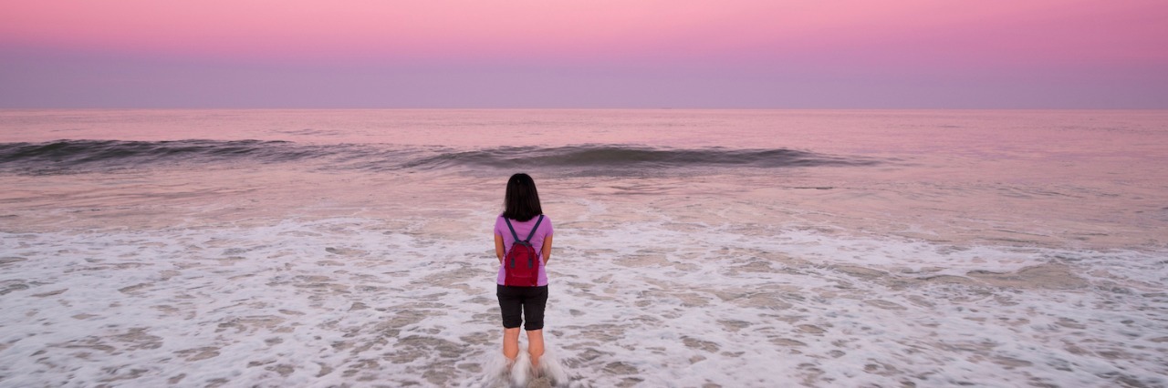 Struggling With My Epilepsy Diagnosis Today and Why That's OK Woman standing in the ocean in front of a pink and purple sky
