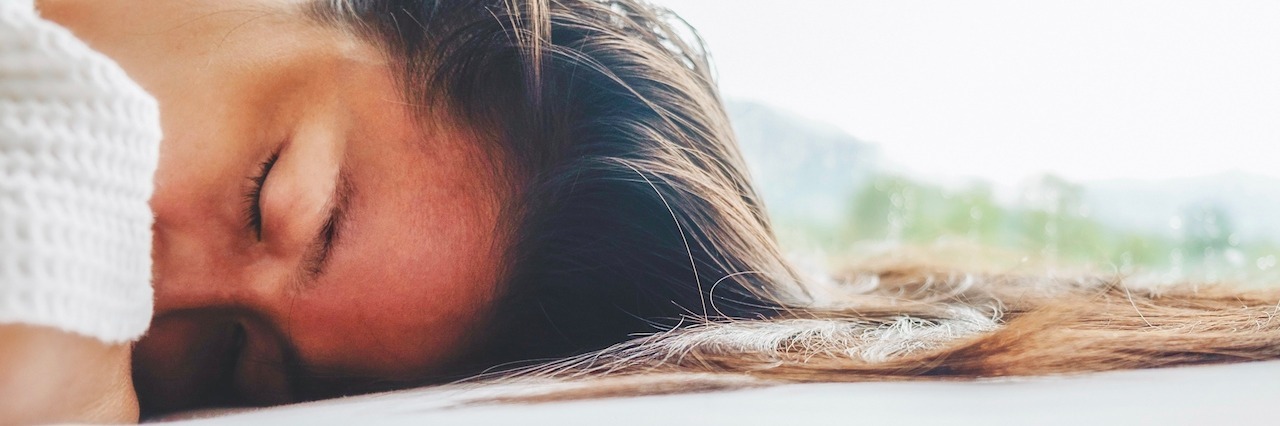 How to Decide Where to Spend Energy If You're Sick brunette long hair woman lies on white bed linen in soft morning light