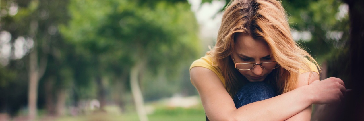 Irrational Survivor's Guilt After a Loved One's Suicide sad blonde woman sitting alone in forest