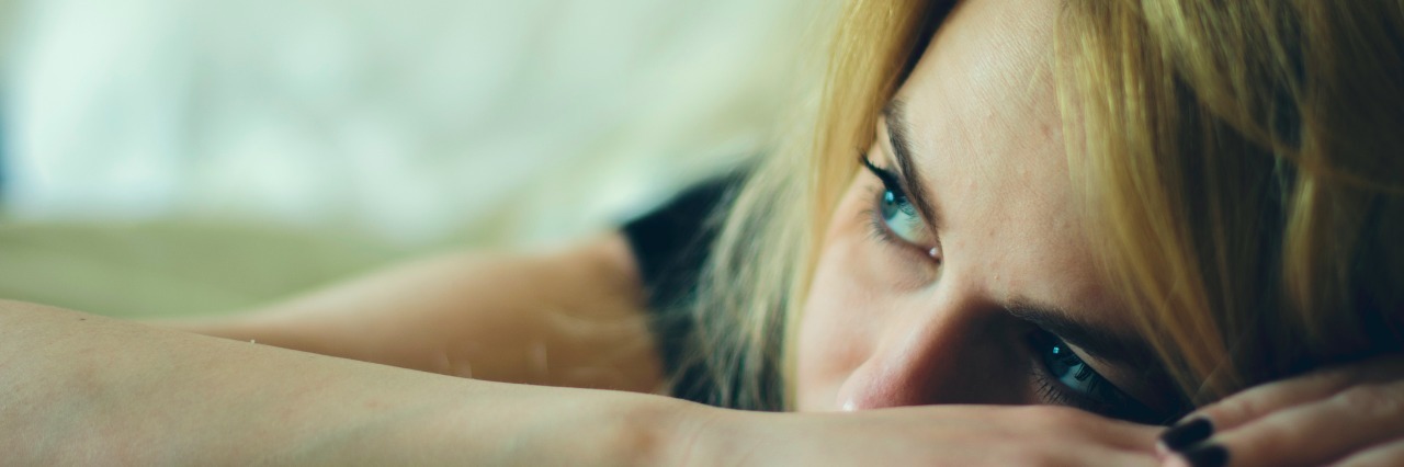 The Side Effects of Overexertion When You Have a Chronic Illness woman laying down in a bed with face on hand