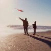 Silhouette of a father and son flying a kite on the beach.