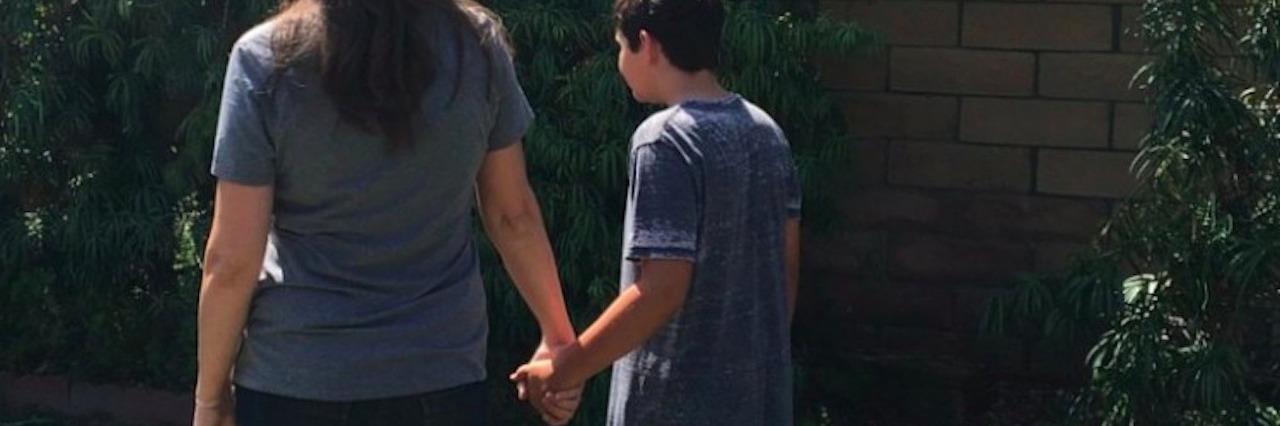 a mom holding hands with her son standing outside