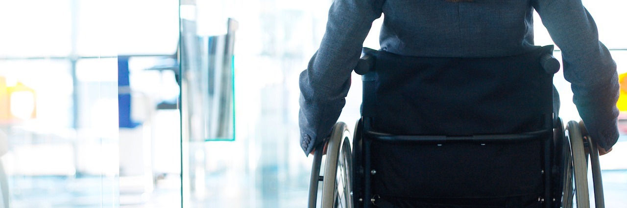 Why Needing to Lie Down Because of POTS Is Not Giving Up rear view of a businesswoman sitting in a wheelchair in an office