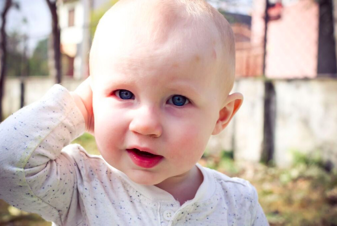 Baby ourdoors, holding one hand up to face