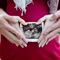 Two pairs of hands on a pregnant woman's stomach, holding an ultrasound photo