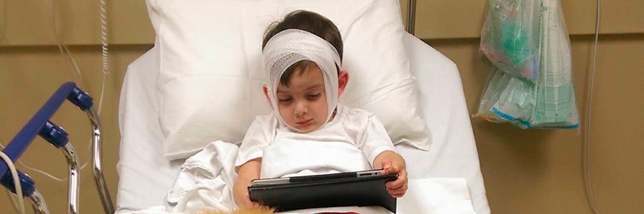 I Am Not a Supermom Because My Son Has Rare Neurological Conditions little boy in a hospital bed with a service dog