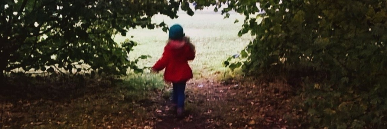 Letter to the Parent of an Undiagnosed Autistic Girl A photo of a child wearing a red jacket, walking through a tree-lined path in a park