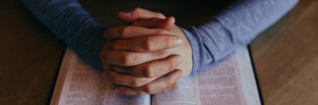 mans hands folded in prayer over his Bible