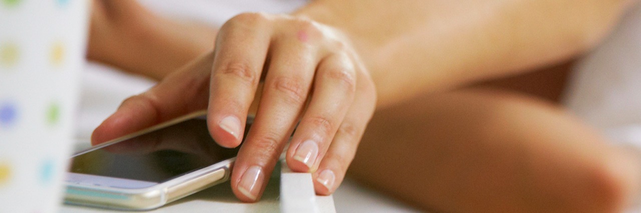 Why I'm Leaving Social Media as Someone With a Chronic Illness Woman Lying In Bed Reaching To Check Mobile Phone