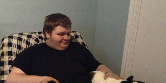 young man sitting in chair with two cats